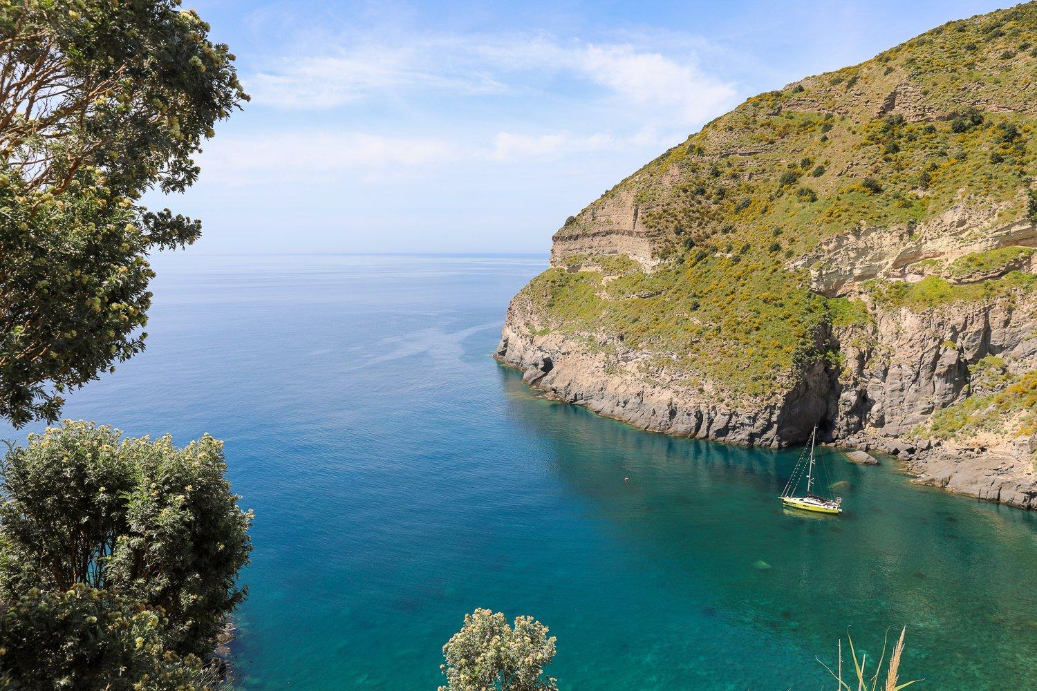 Sailboat roaming around the waters of Baia di Sorgeto. In this guide to Ischia, Italy, you'll find the best things to do and other must-know tips before you go!